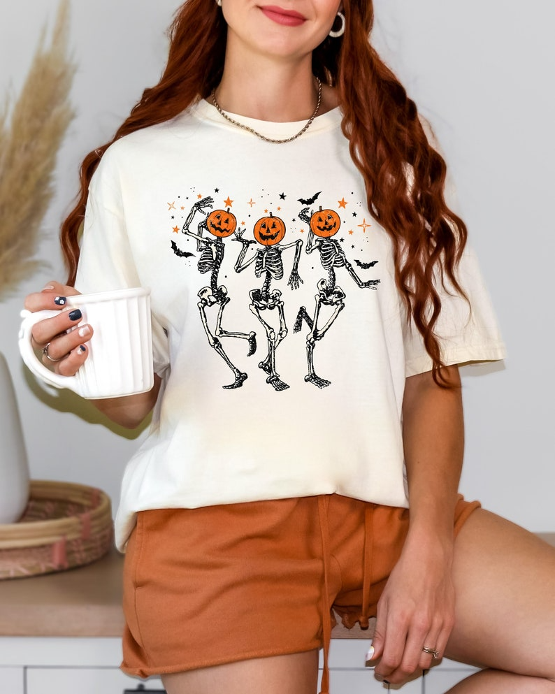 a woman holding a coffee cup and wearing a halloween t - shirt