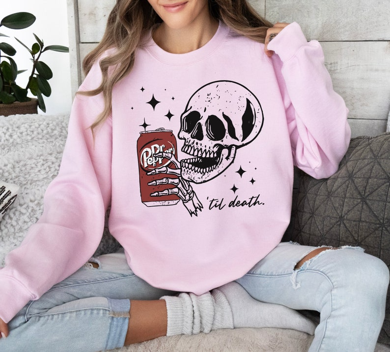 a woman sitting on a couch wearing a pink sweatshirt