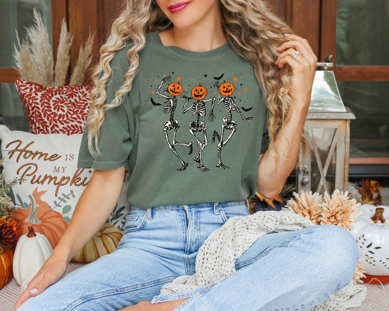 a woman sitting on the floor wearing a t - shirt with skeletons and pumpkins